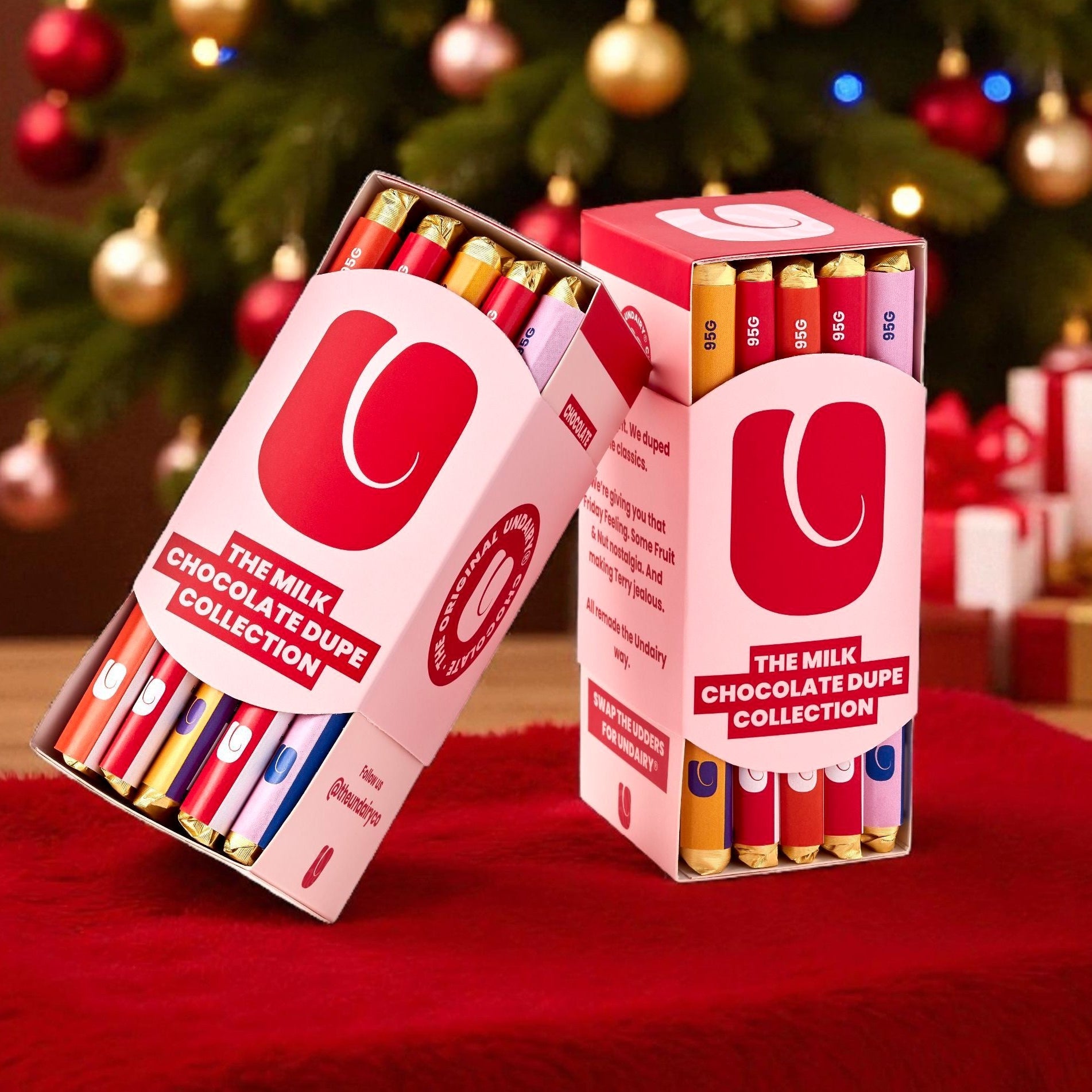 Two boxes of chocolate dupe collection in front of a decorated Christmas tree with presents.